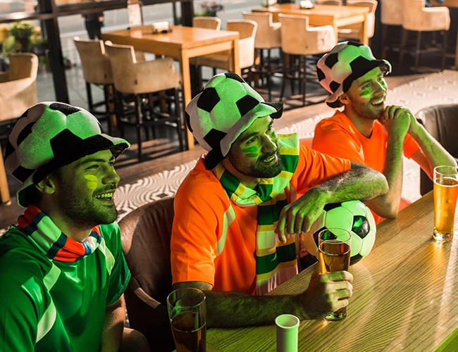 Aficionados viendo futbol en un restaurante con cerveza en mano 