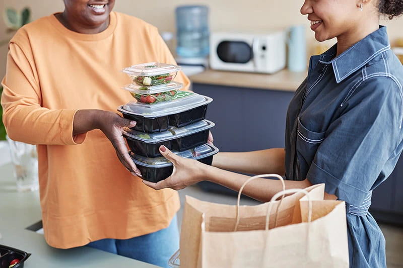 blog woman passing stack of takeout containers to anoth